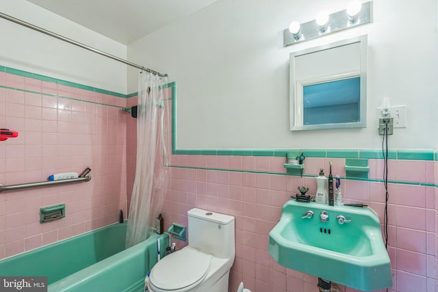 full bathroom featuring toilet, a sink, shower / bath combo, tile walls, and a wainscoted wall