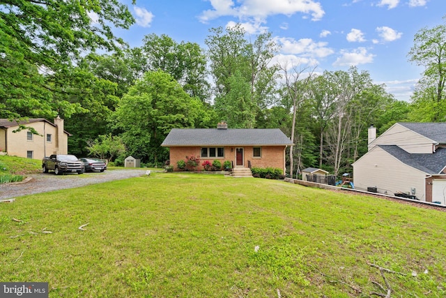 view of front facade featuring driveway, a storage unit, brick siding, a front lawn, and a chimney