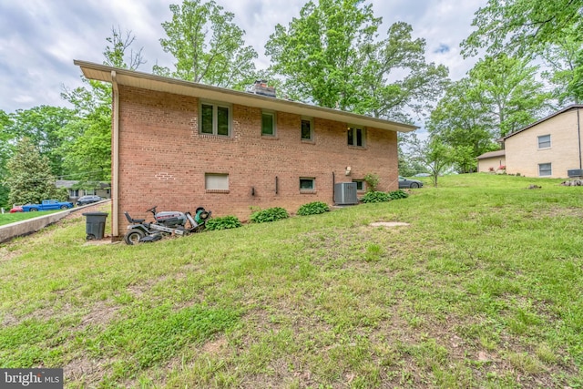 rear view of house with cooling unit, brick siding, a yard, and a chimney