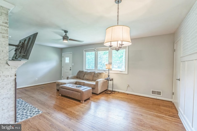 living room with a ceiling fan, wood finished floors, baseboards, and a brick fireplace