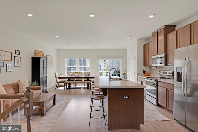 kitchen with appliances with stainless steel finishes, a sink, a center island with sink, light wood finished floors, and recessed lighting
