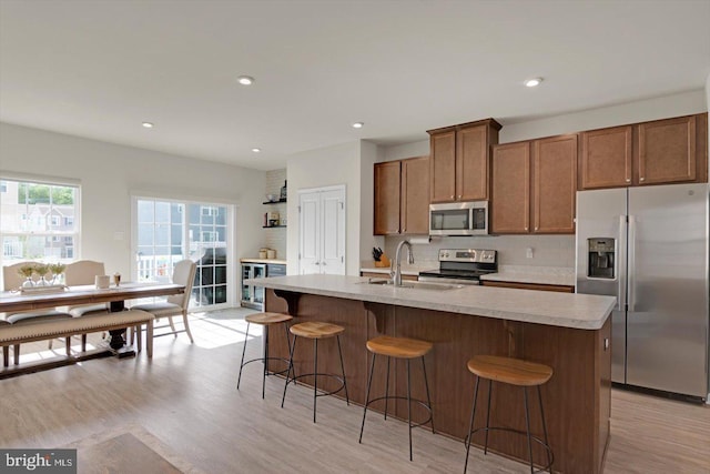 kitchen with appliances with stainless steel finishes, light countertops, brown cabinetry, a sink, and a breakfast bar