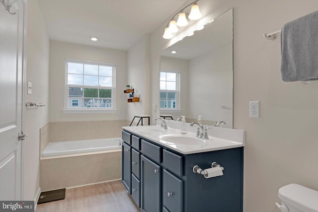 bathroom featuring wood finished floors, a bath, toilet, and double vanity
