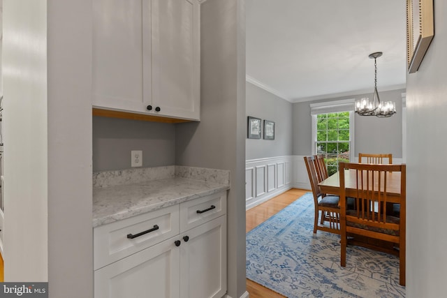 7071 Garden Walk, Columbia, MD 21044 - kitchen with crown molding, light wood-style flooring, white cabinets, a wainscoted wall, and a chandelier