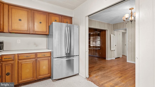 kitchen featuring freestanding refrigerator, ornamental molding, brown cabinets, a chandelier, and light countertops