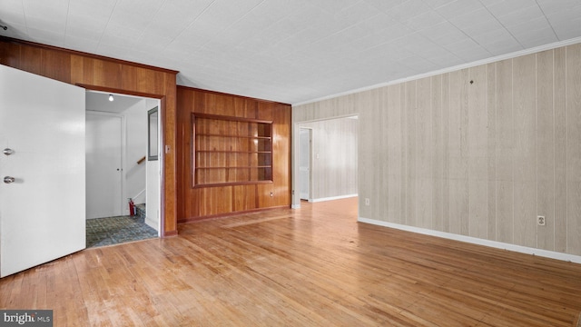 spare room with wood walls, crown molding, built in features, wood finished floors, and baseboards