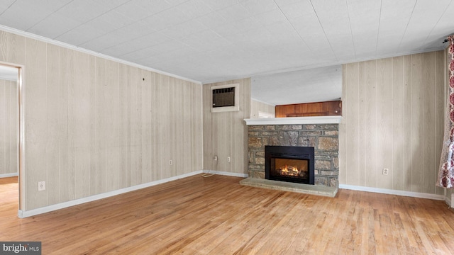 unfurnished living room with wood finished floors, a fireplace, wooden walls, crown molding, and baseboards
