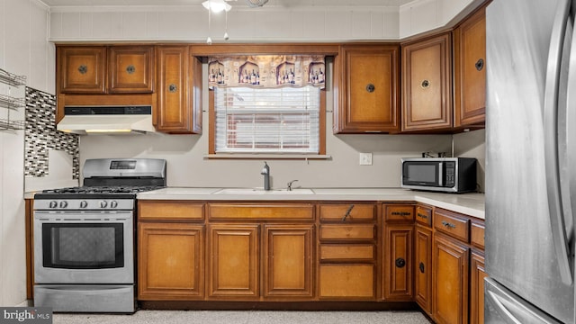kitchen with stainless steel appliances, a sink, under cabinet range hood, brown cabinetry, and ornamental molding