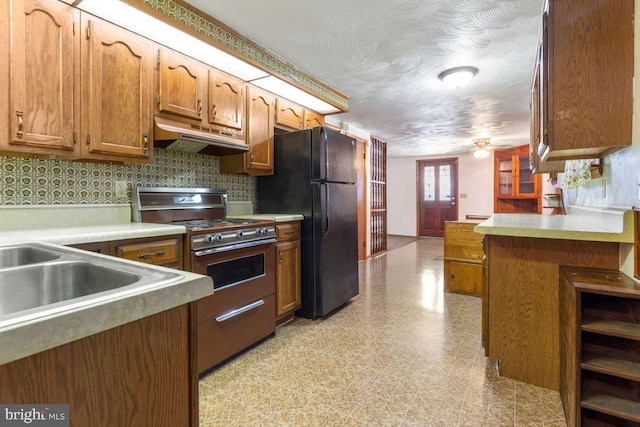 449 Carlisle St, Hanover, PA 17331 - kitchen featuring stainless steel range with gas cooktop, freestanding refrigerator, under cabinet range hood, brown cabinetry, and light countertops