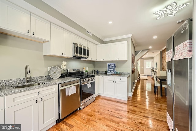 kitchen featuring stainless steel appliances, a sink, ornamental molding, white cabinets, and light stone counters