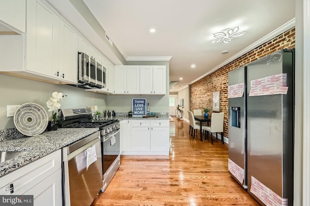kitchen featuring appliances with stainless steel finishes, ornamental molding, brick wall, white cabinetry, and light stone countertops