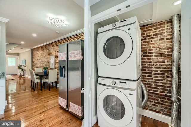 laundry area featuring brick wall, estacked washer and dryer, crown molding, light wood-style floors, and baseboards