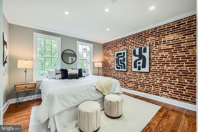 bedroom featuring brick wall, ornamental molding, baseboards, wood finished floors, and an accent wall