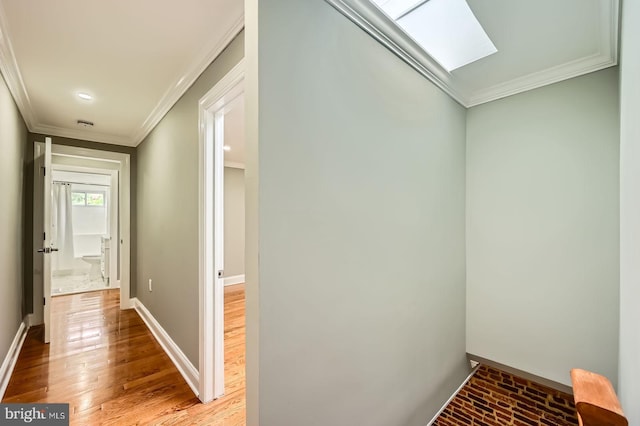 corridor with ornamental molding, baseboards, a skylight, light wood finished floors, and recessed lighting