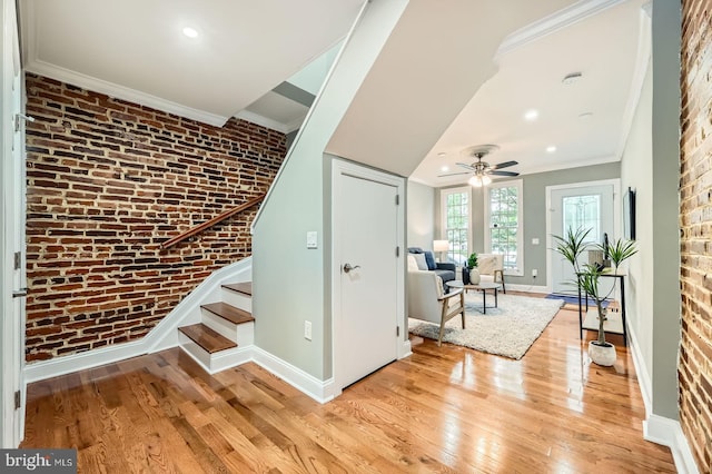 entryway with crown molding, baseboards, light wood-style floors, a ceiling fan, and brick wall
