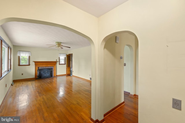 unfurnished living room featuring ceiling fan, wood-type flooring, baseboards, and a fireplace with flush hearth