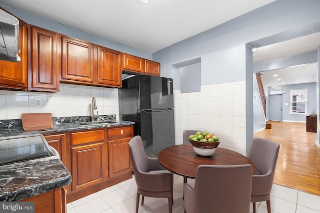 kitchen featuring a sink, freestanding refrigerator, tile walls, brown cabinetry, and light tile patterned flooring