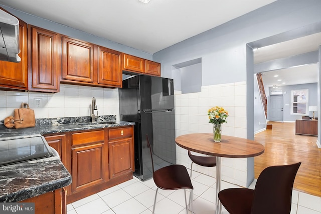 kitchen with freestanding refrigerator, a sink, tile walls, brown cabinets, and light tile patterned floors