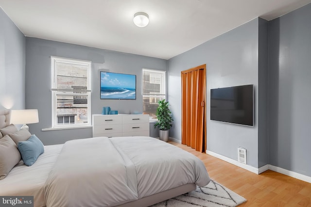 bedroom with multiple windows, light wood-type flooring, and baseboards