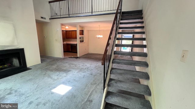 stairway with a fireplace with flush hearth, carpet, a chandelier, and a high ceiling