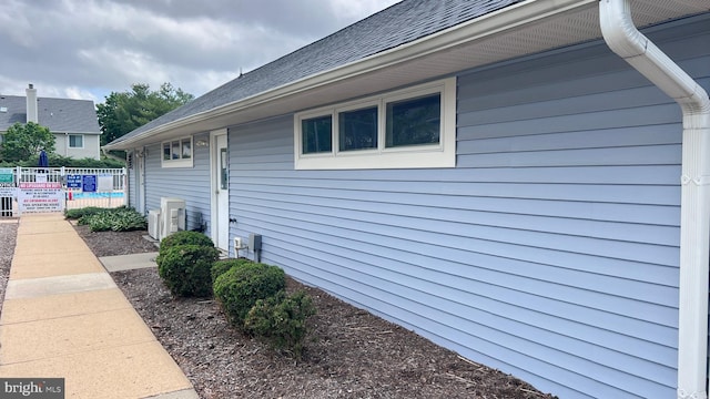 view of side of home with fence, a shingled roof, and ac unit