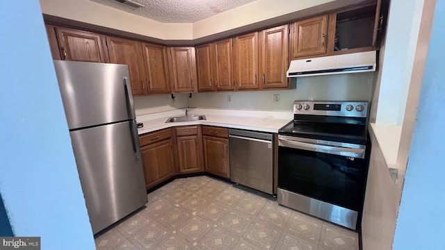kitchen featuring stainless steel appliances, range hood, brown cabinetry, a sink, and a textured ceiling