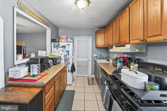 kitchen featuring under cabinet range hood, freestanding refrigerator, range with gas stovetop, light tile patterned floors, and a sink