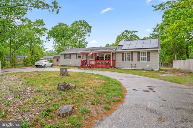 ranch-style home with curved driveway, a porch, and roof mounted solar panels