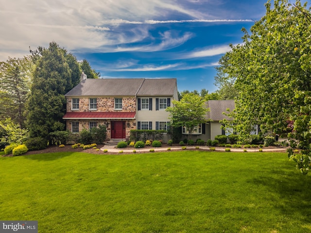 view of front of house featuring a front yard, stone siding, a chimney, and a standing seam roof