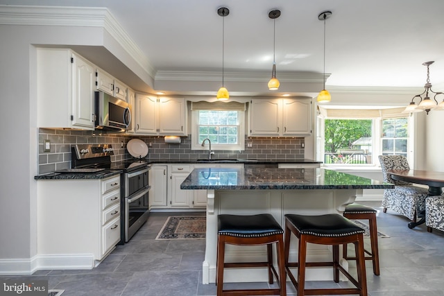 kitchen featuring appliances with stainless steel finishes, a sink, ornamental molding, a kitchen breakfast bar, and white cabinets
