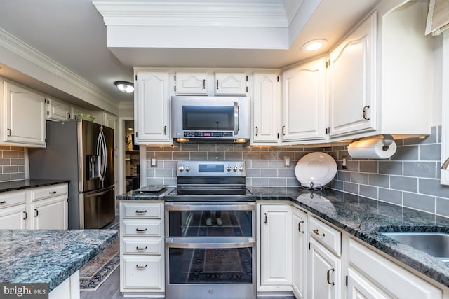 kitchen with appliances with stainless steel finishes, tasteful backsplash, crown molding, white cabinets, and dark stone counters