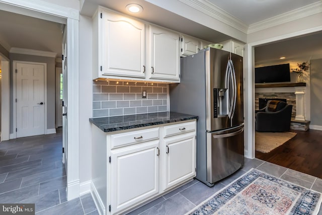kitchen with stainless steel fridge with ice dispenser, dark stone countertops, white cabinets, crown molding, and backsplash