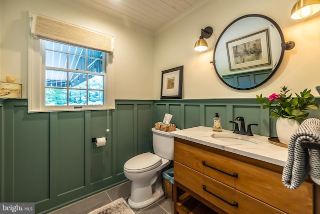 bathroom with a decorative wall, tile patterned floors, crown molding, vanity, and a wainscoted wall