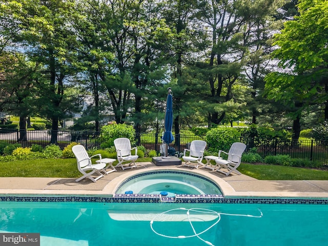 view of pool with fence and a pool with connected hot tub