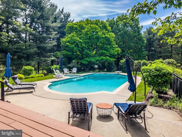 view of swimming pool with fence, a patio area, and view of wooded area