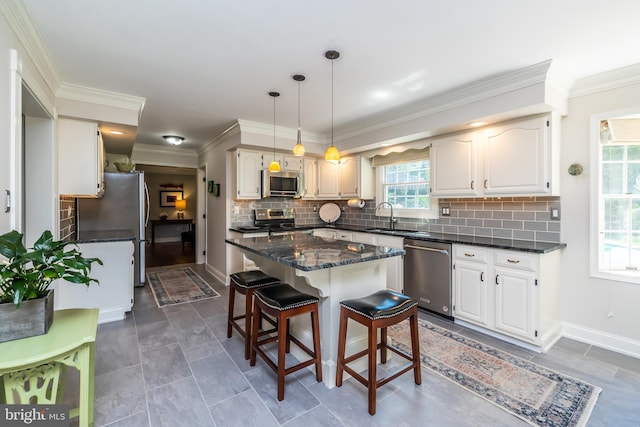 kitchen with stainless steel appliances, a sink, a center island, tasteful backsplash, and ornamental molding