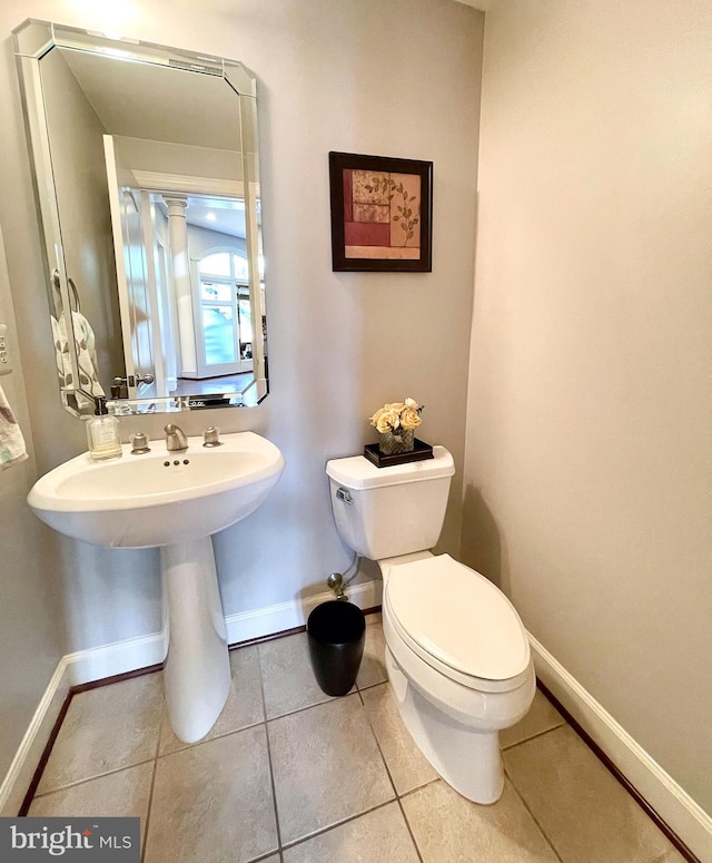 half bath with baseboards, toilet, tile patterned floors, and a sink