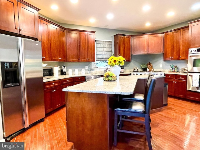 kitchen with appliances with stainless steel finishes, a kitchen island, light wood-type flooring, a breakfast bar, and light stone countertops