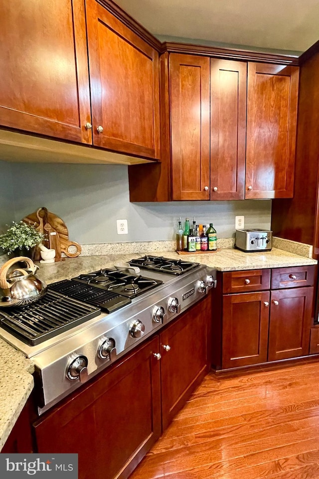 kitchen with stainless steel gas stovetop, light wood-style floors, and light stone countertops