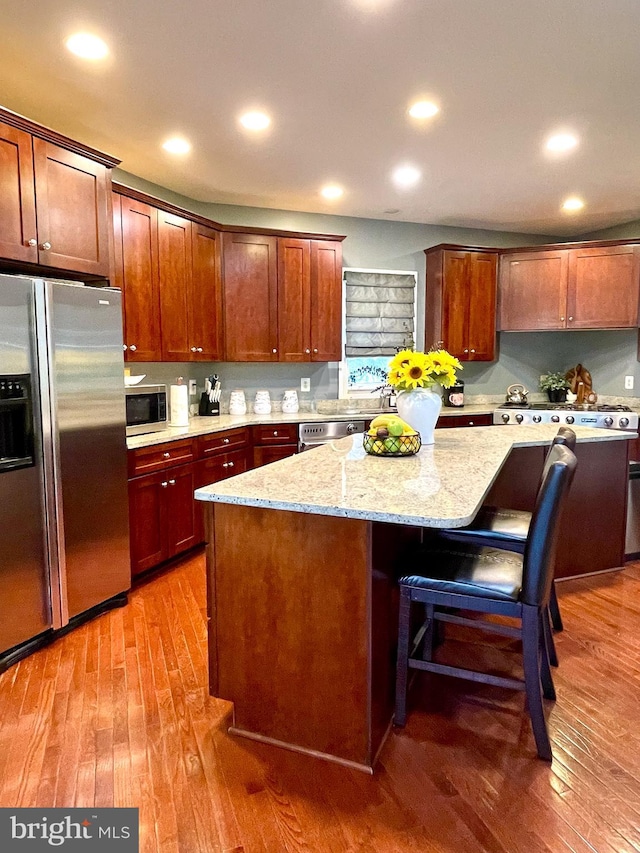 kitchen with appliances with stainless steel finishes, a kitchen island, light wood-style floors, light stone countertops, and a kitchen breakfast bar