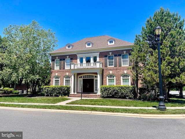 colonial-style house with brick siding, a balcony, and a front lawn