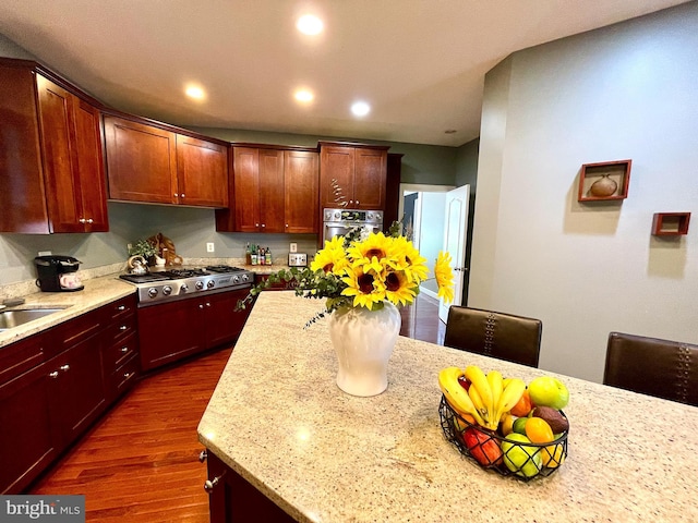 kitchen with appliances with stainless steel finishes, dark wood finished floors, light stone countertops, recessed lighting, and a sink