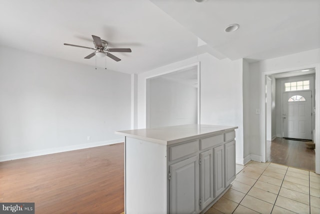 kitchen featuring a ceiling fan, baseboards, light countertops, light wood-type flooring, and a kitchen island