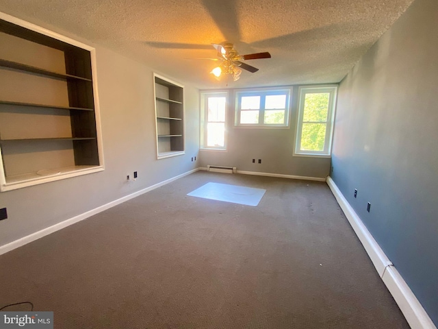 carpeted empty room with a textured ceiling, a baseboard heating unit, a ceiling fan, built in shelves, and baseboards