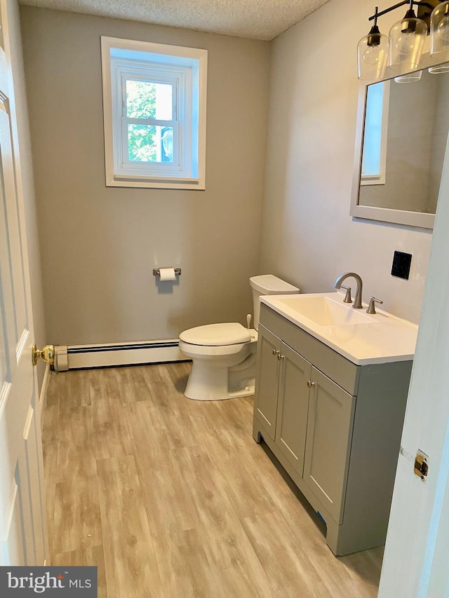 bathroom with a baseboard heating unit, a textured ceiling, toilet, vanity, and wood finished floors