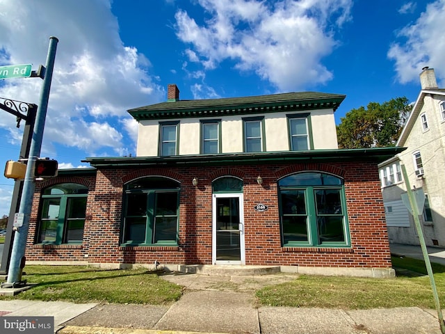 view of front facade featuring stucco siding, brick siding, and a chimney
