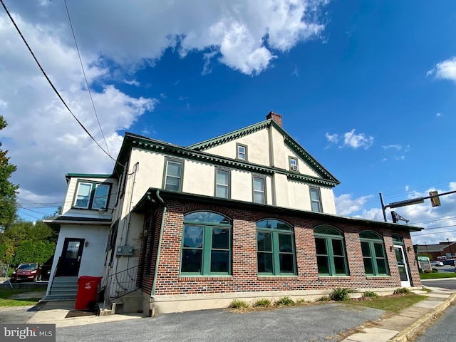 view of side of home featuring stucco siding, entry steps, a chimney, and brick siding