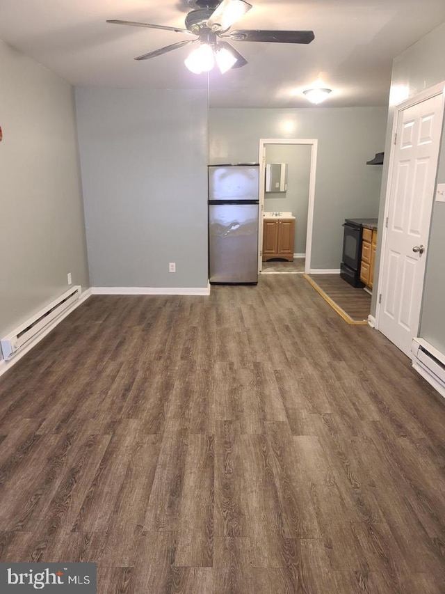 spare room with a baseboard heating unit, a wood stove, dark wood-type flooring, ceiling fan, and baseboards
