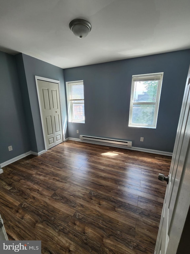 unfurnished bedroom with a baseboard heating unit, baseboards, a closet, and dark wood finished floors