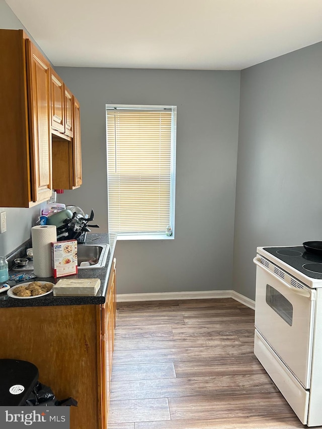 kitchen featuring electric stove, wood finished floors, brown cabinetry, baseboards, and dark countertops